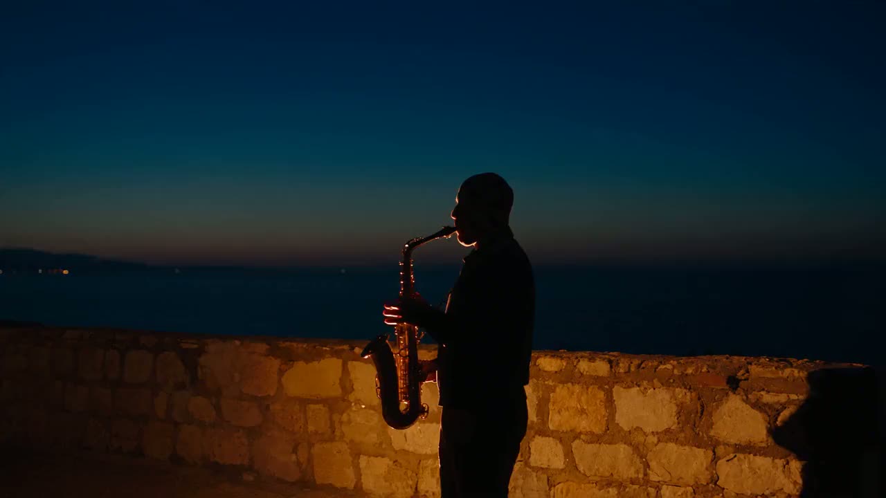 Saxophonist silhouetted against the dusk sea